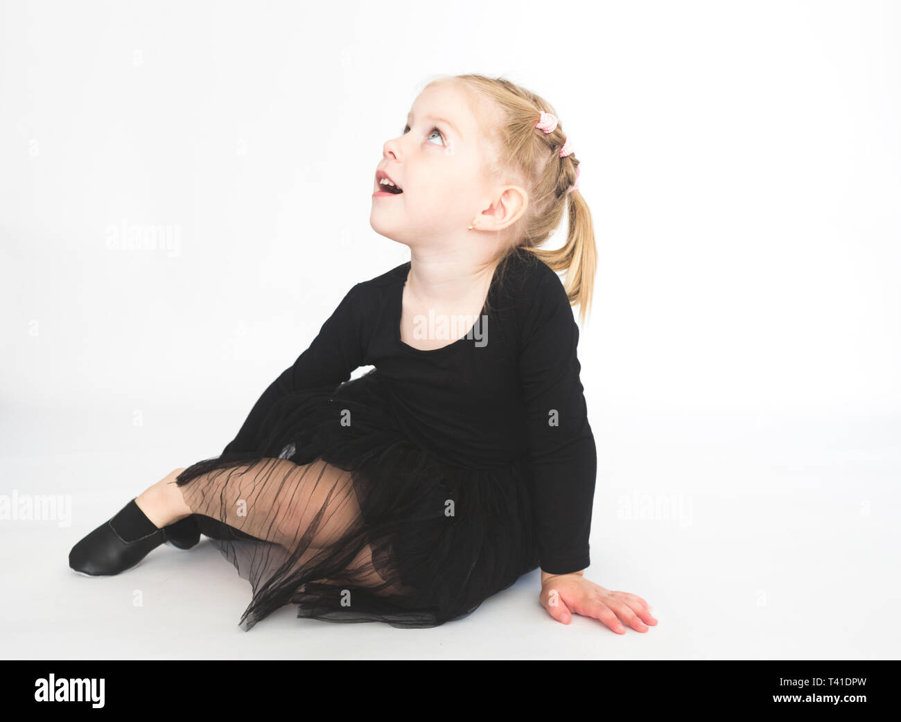 Cute little girl in beautiful black dress sitting on the floor on white ...