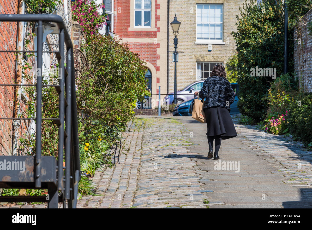 A woman walking up a steep hill in Tarrant Street, a cobbled road in Arundel, West Sussex, England, UK. Stock Photo