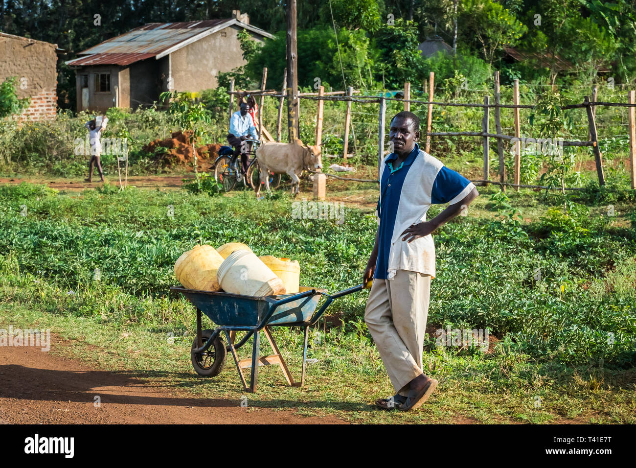 near Kisumu, Kenya - March 8, 2019 - a man with a wheelbarrow full of canisters having rest on the roadside on his way to a well to fetch water Stock Photo