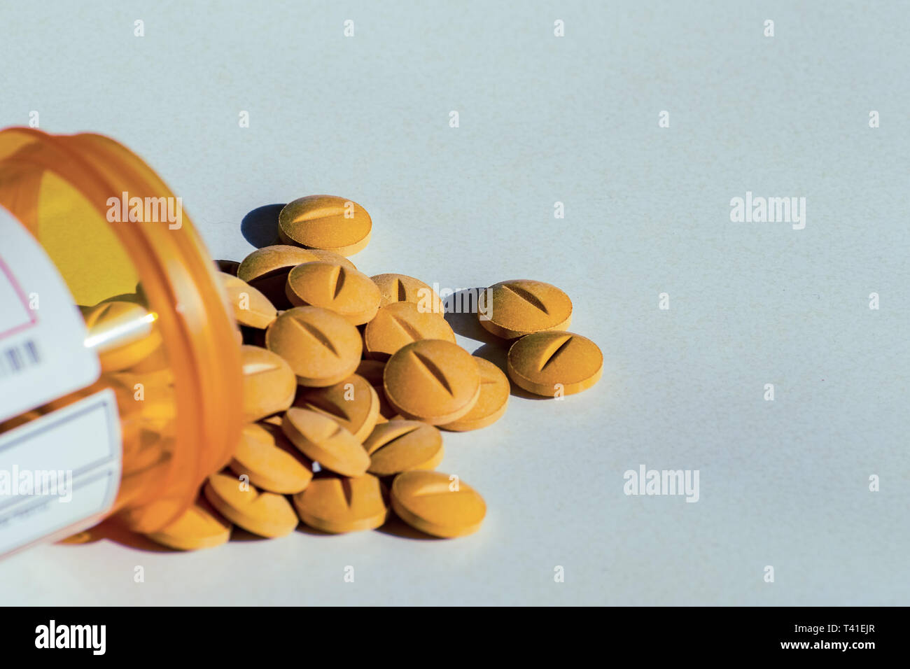 Yellow prescription pills spilled onto a table. Concept of opioid addiction and healthcare industry Stock Photo