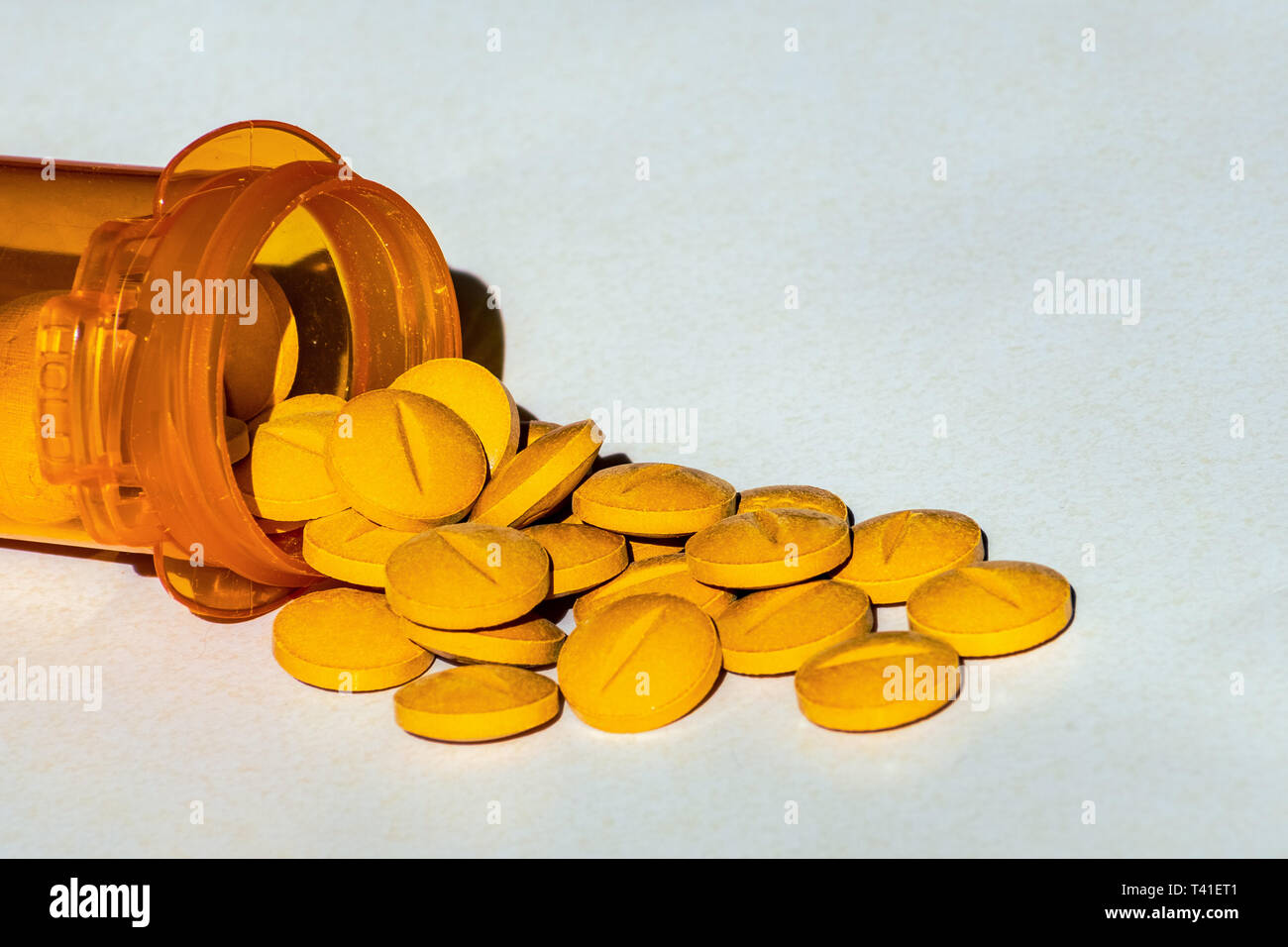 Yellow prescription pills spilled onto a table. Concept of opioid addiction and healthcare industry Stock Photo