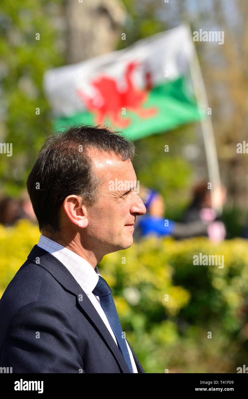 Alun Cairns MP (Con; Secretary of State for Wales) on College Green, Westminster, April 11th 2019 A Welsh flag behind, carried by a pro-EU protester i Stock Photo