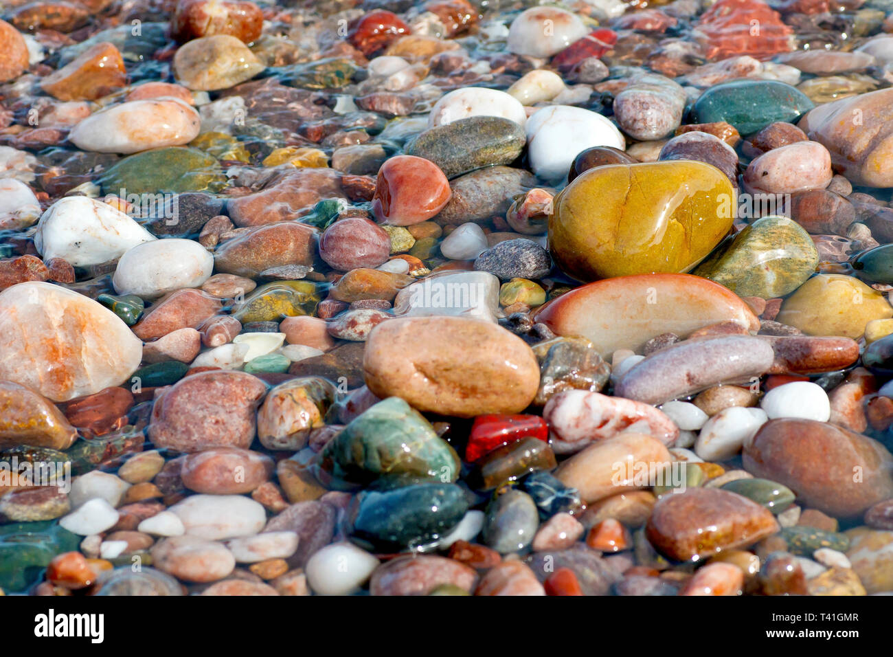 Pebbles left wet and colourful on the beach as a wave ebbs away from the shore. Stock Photo