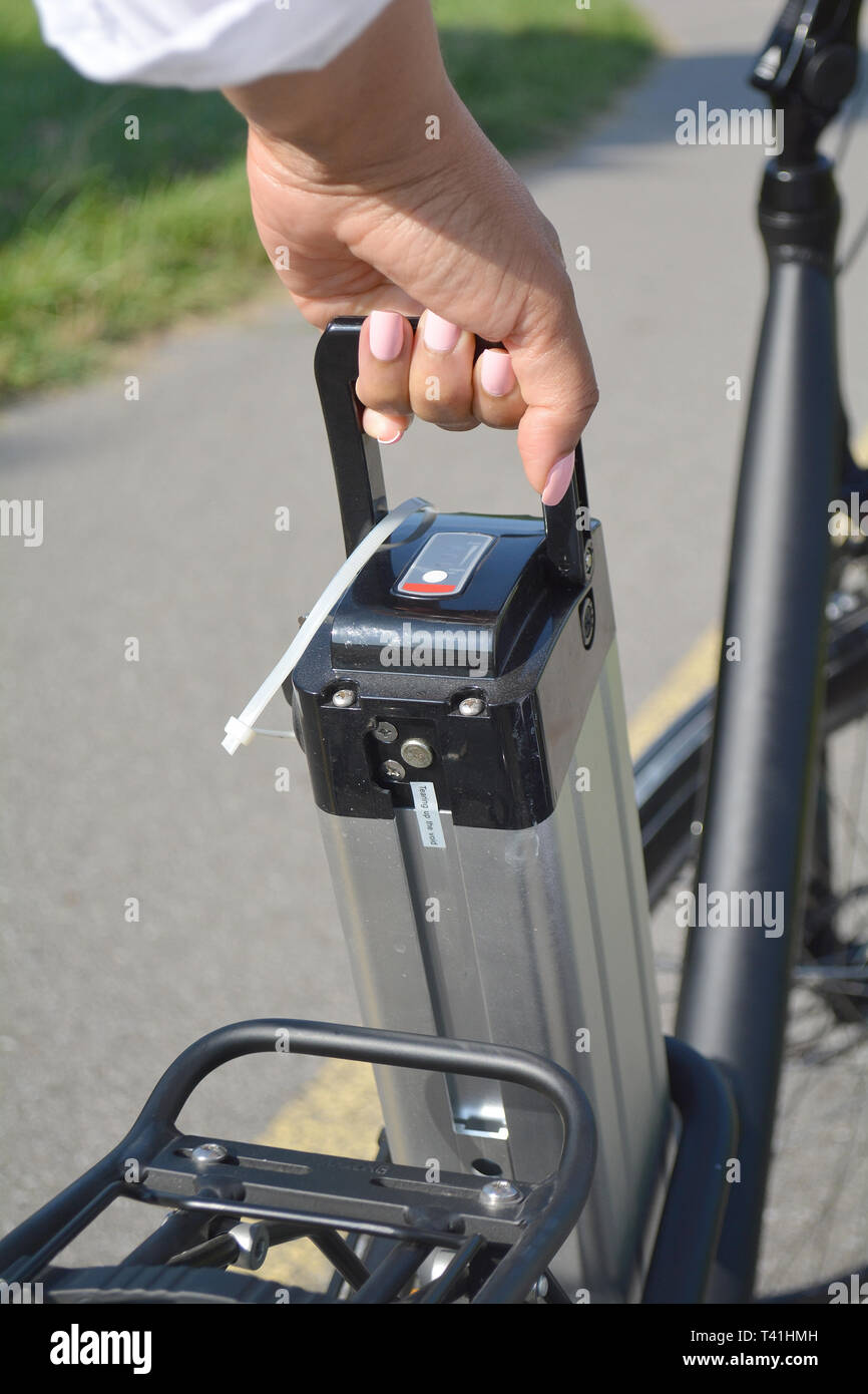 Women holding battery pack of electric bicycle near her e bike. Female