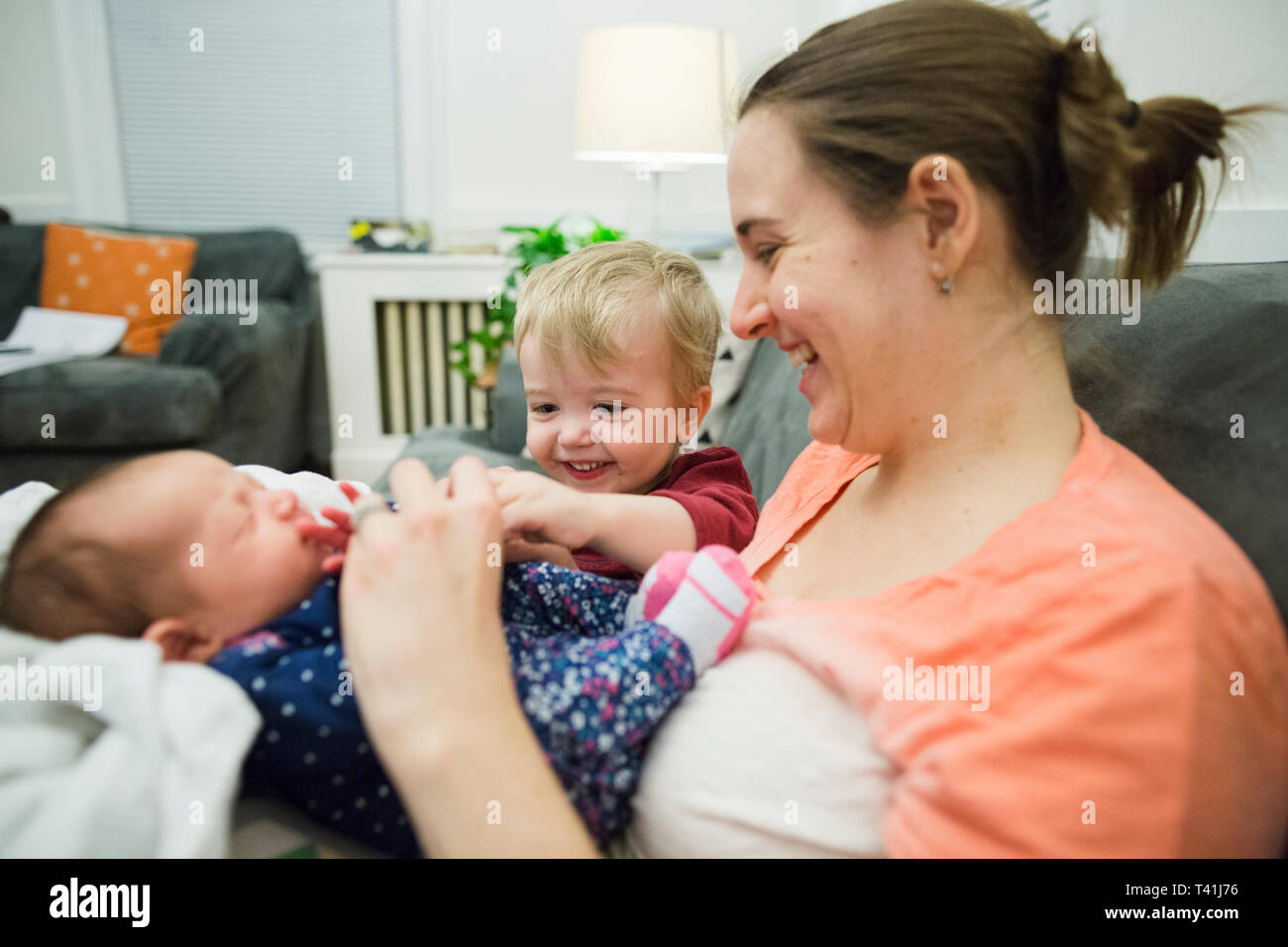 Happy blonde boy sits next to new mother and newborn baby girl at home Stock Photo