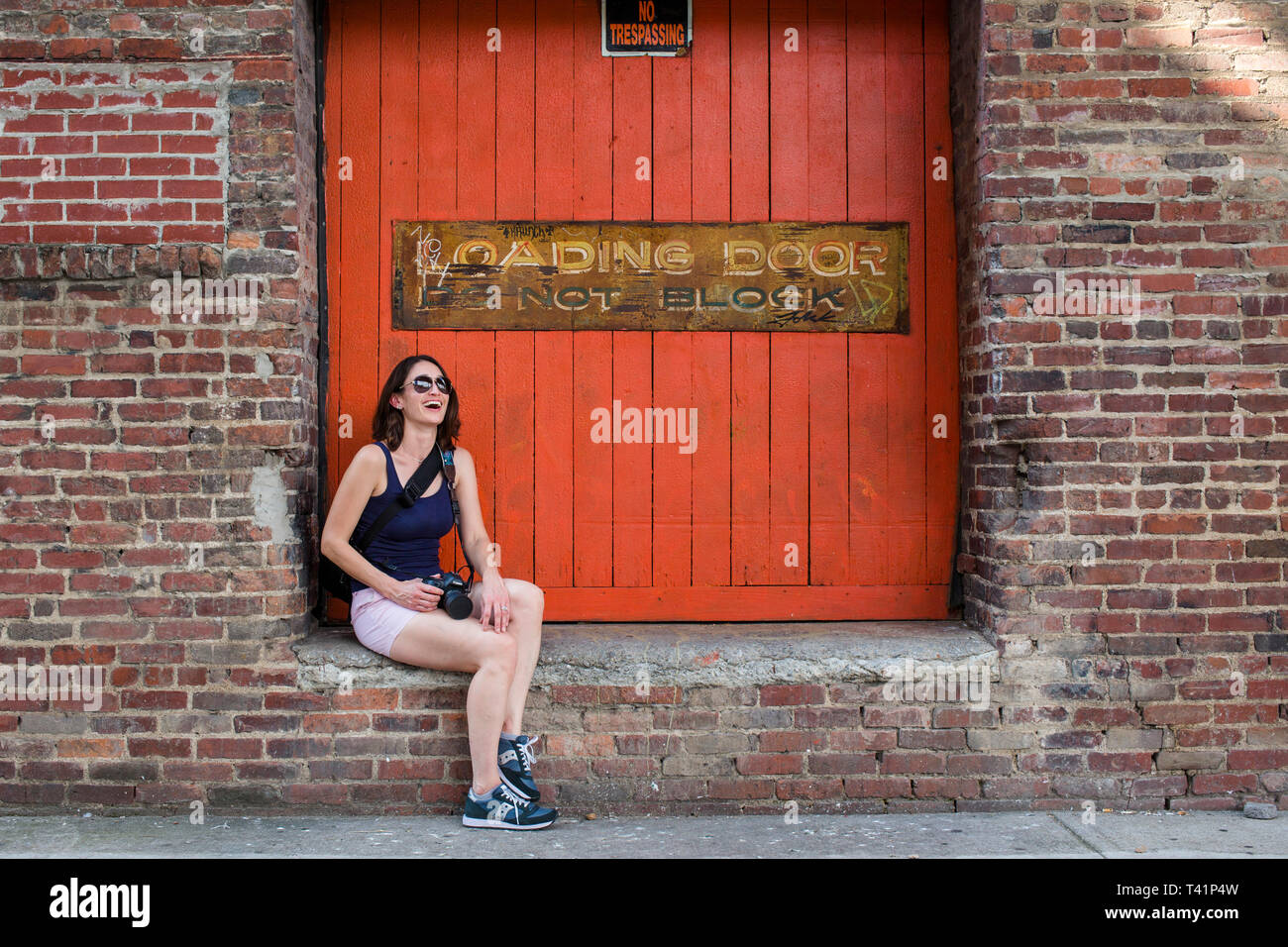 a laughing woman tourist sits on a brick wall in an alley Stock Photo