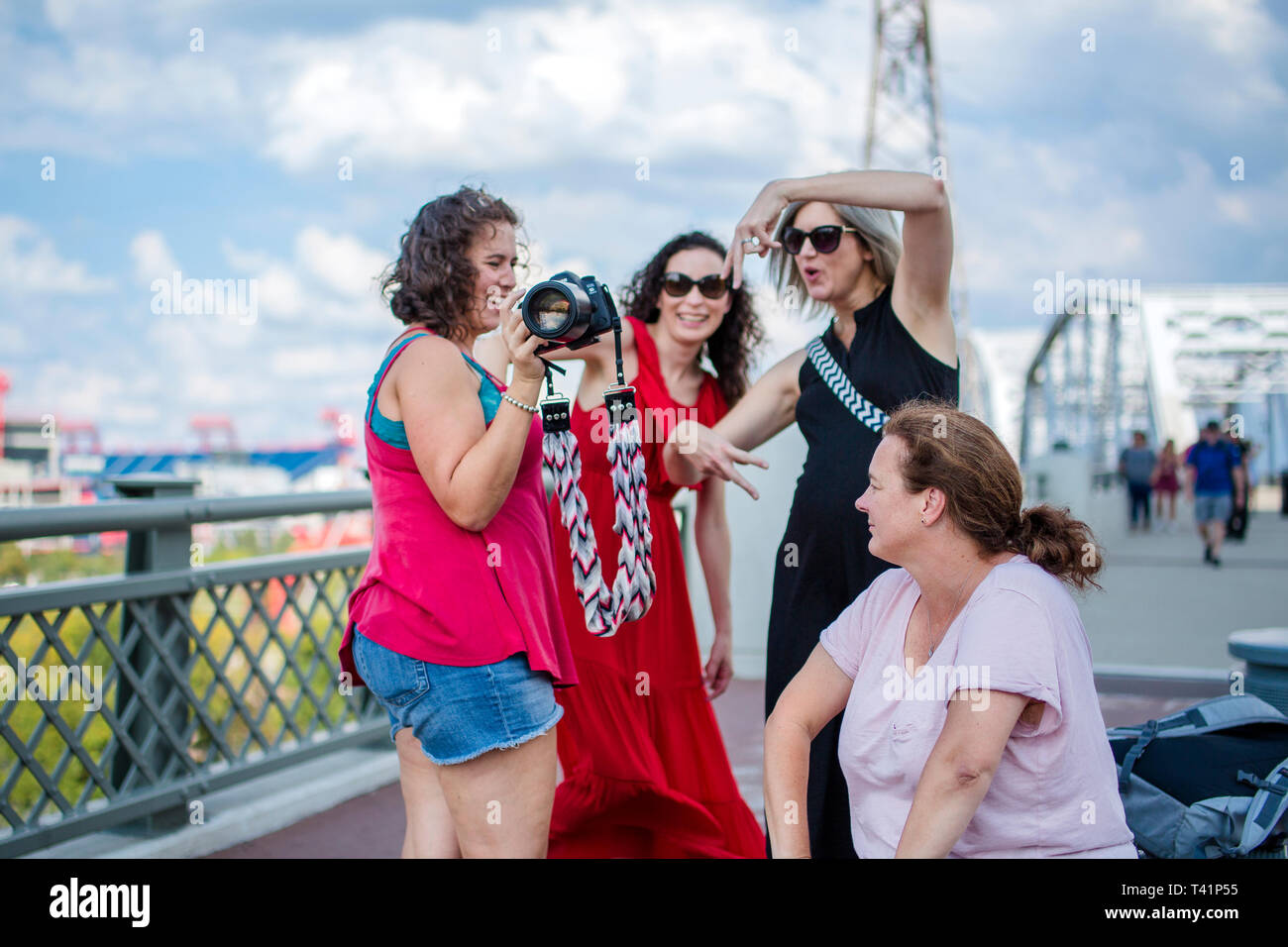 a group of laughing women friends pose for pictures on a bridge Stock Photo