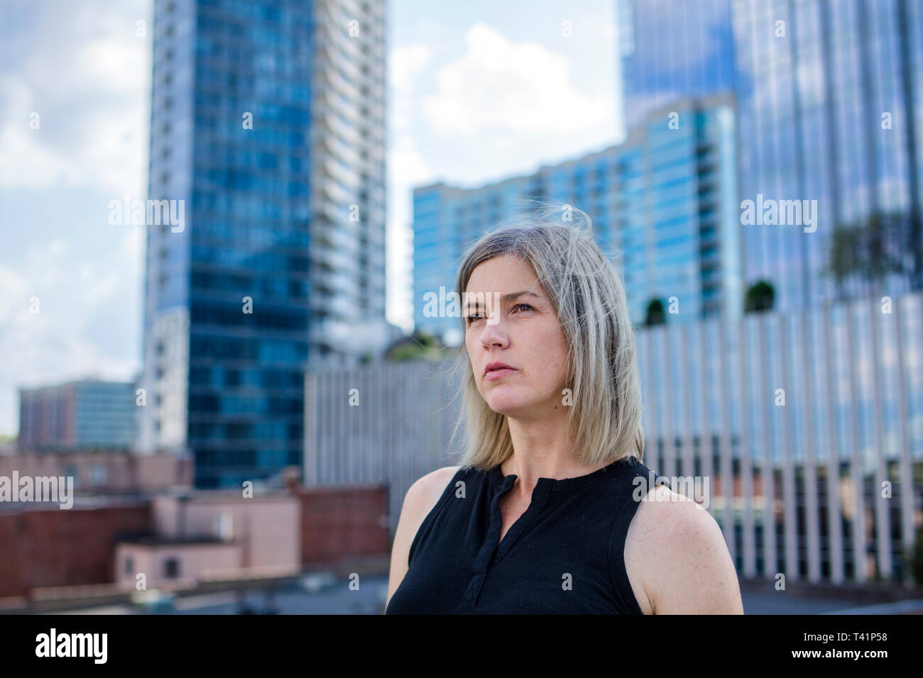 a beautiful woman stands in front of skyscrapers looking into distance Stock Photo