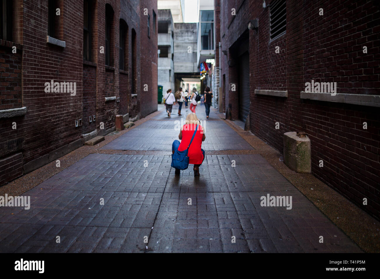 a woman photographer crouches in an alley taking a picture of friends Stock Photo