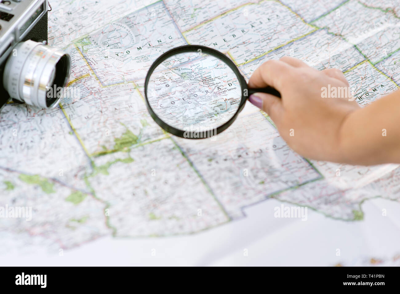 The hand of a woman points her magnifying glass at a map to plan her travels Stock Photo