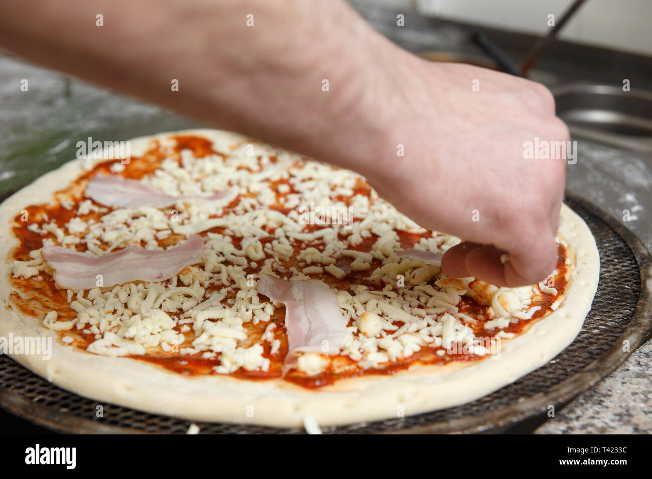 The hands of chef sprinkles the pizza with cheese in restaurant kitchen