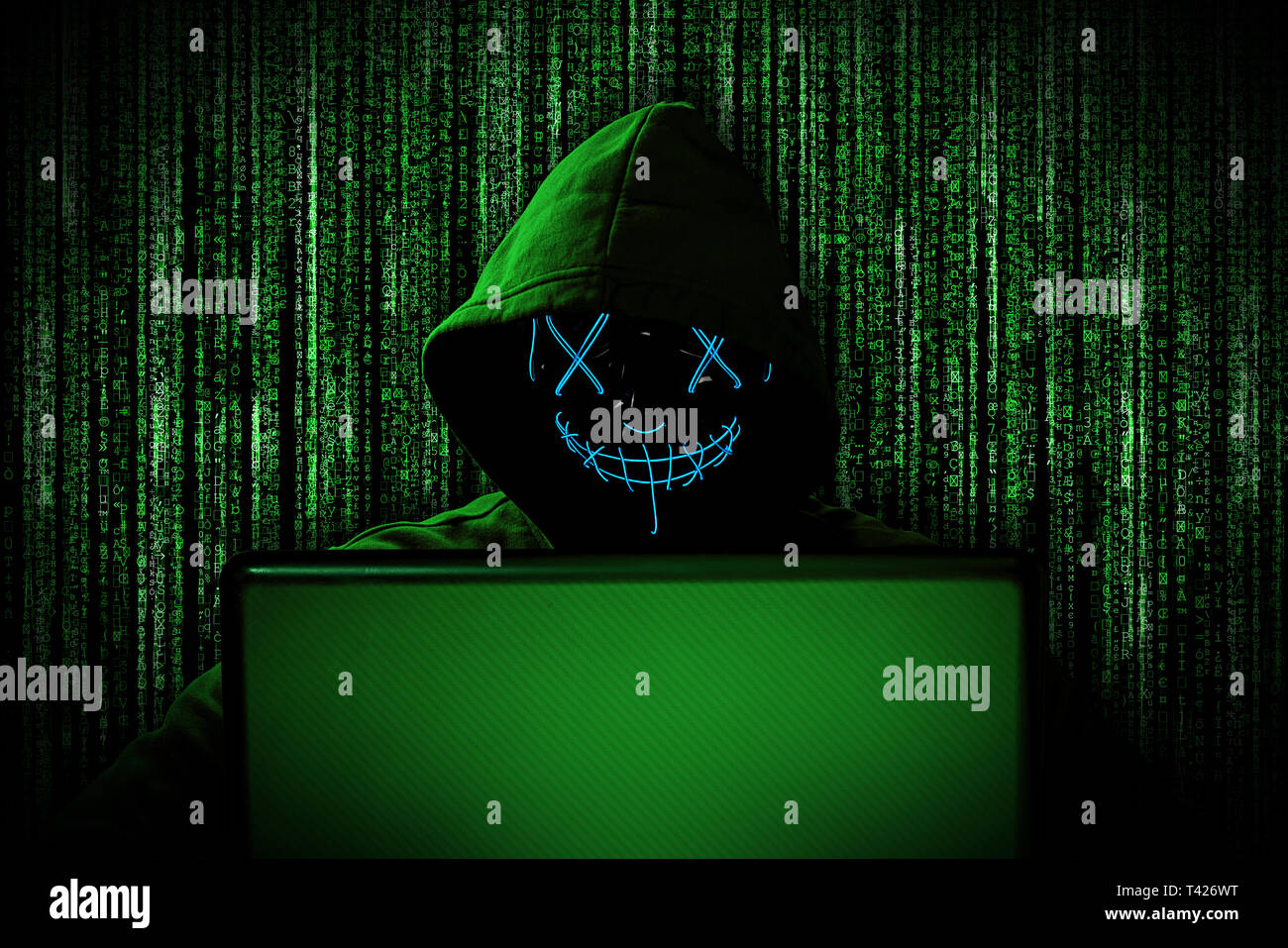 hacker with glowing mask behind notebook laptop in front of green source binary code background internet cyber hack attack computer concept Stock Photo