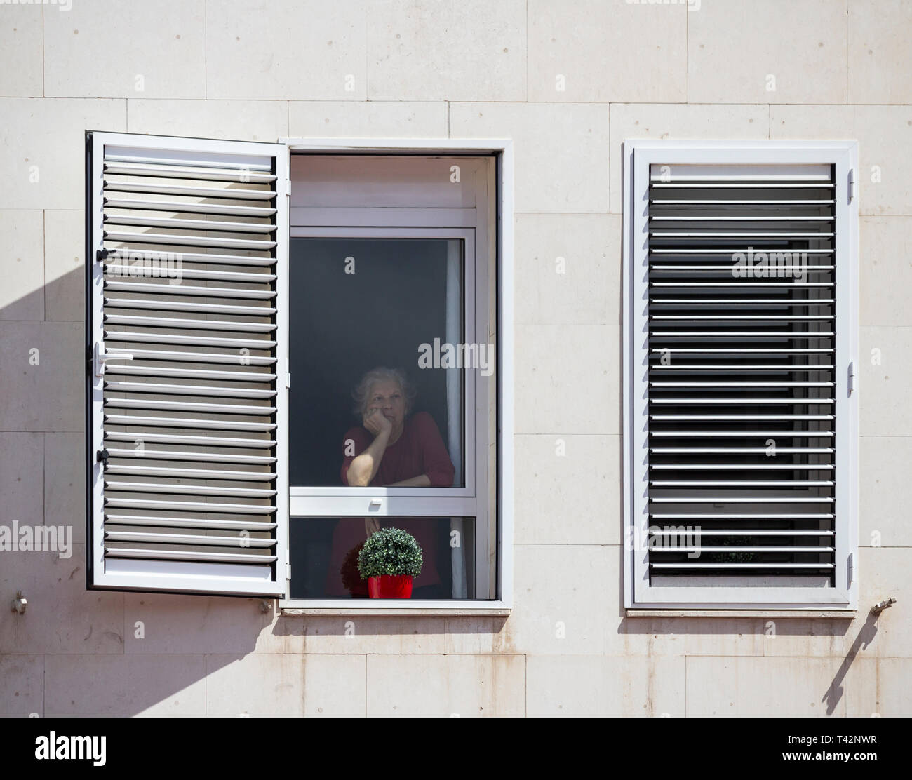 Elderly woman looking out of window from high rise building in Spain ...