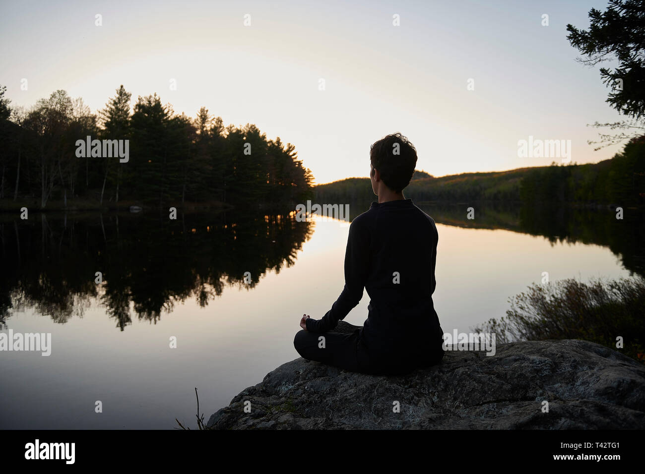 Woman sits cross legged by a lake meditating, Quebec, Canada Stock Photo