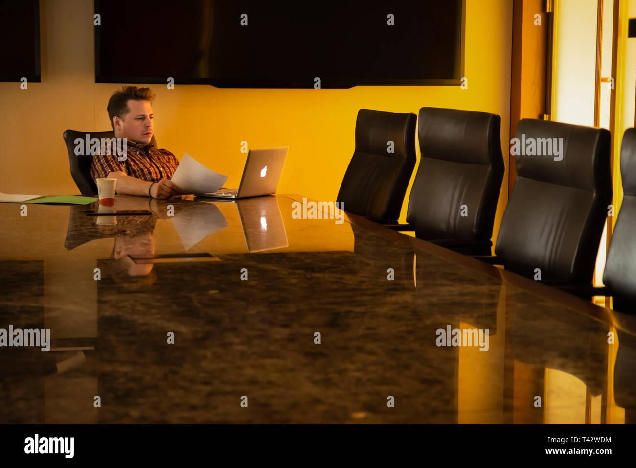 Newark, NJ - April 12, 2019: Man works on laptop at large corporate conference table; late evening or early morning sun shines through window. Stock Photo