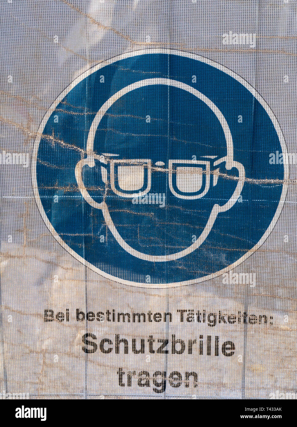 Symbol on a transparent tarpaulin as an indication of safety on a construction site. You can see that you should wear safety goggles. The text means i Stock Photo