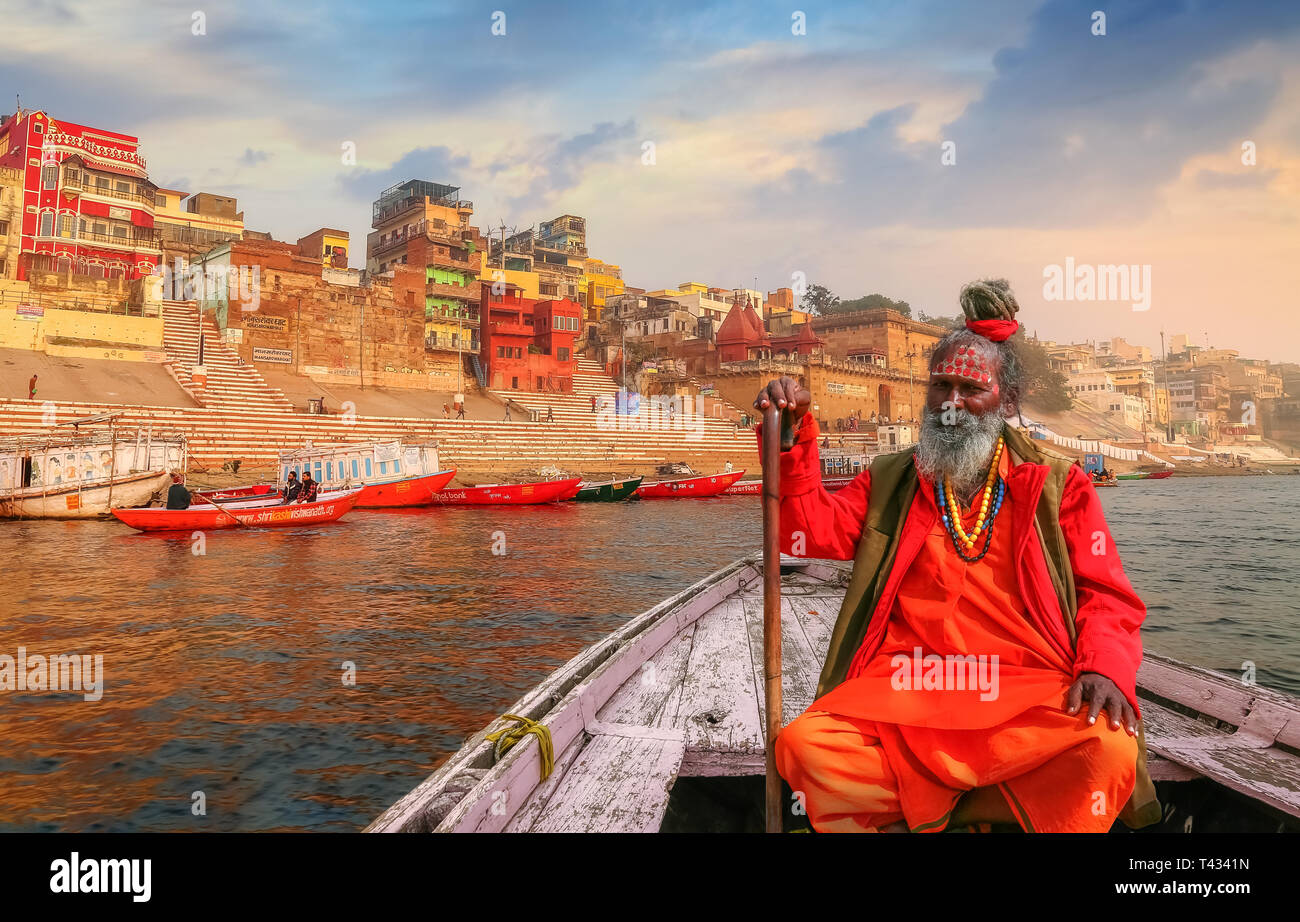 Sadhu baba sitting on a wooden overlooking ancient Varanasi city architecture with Ganges river ghat at sunset. Stock Photo