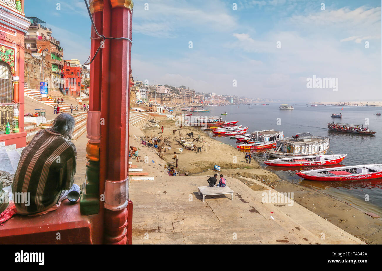 Old man sitting on a temple parapet gets a  panoramic view of the Ganges river bank with ancient architecture at Varanasi, India. Stock Photo