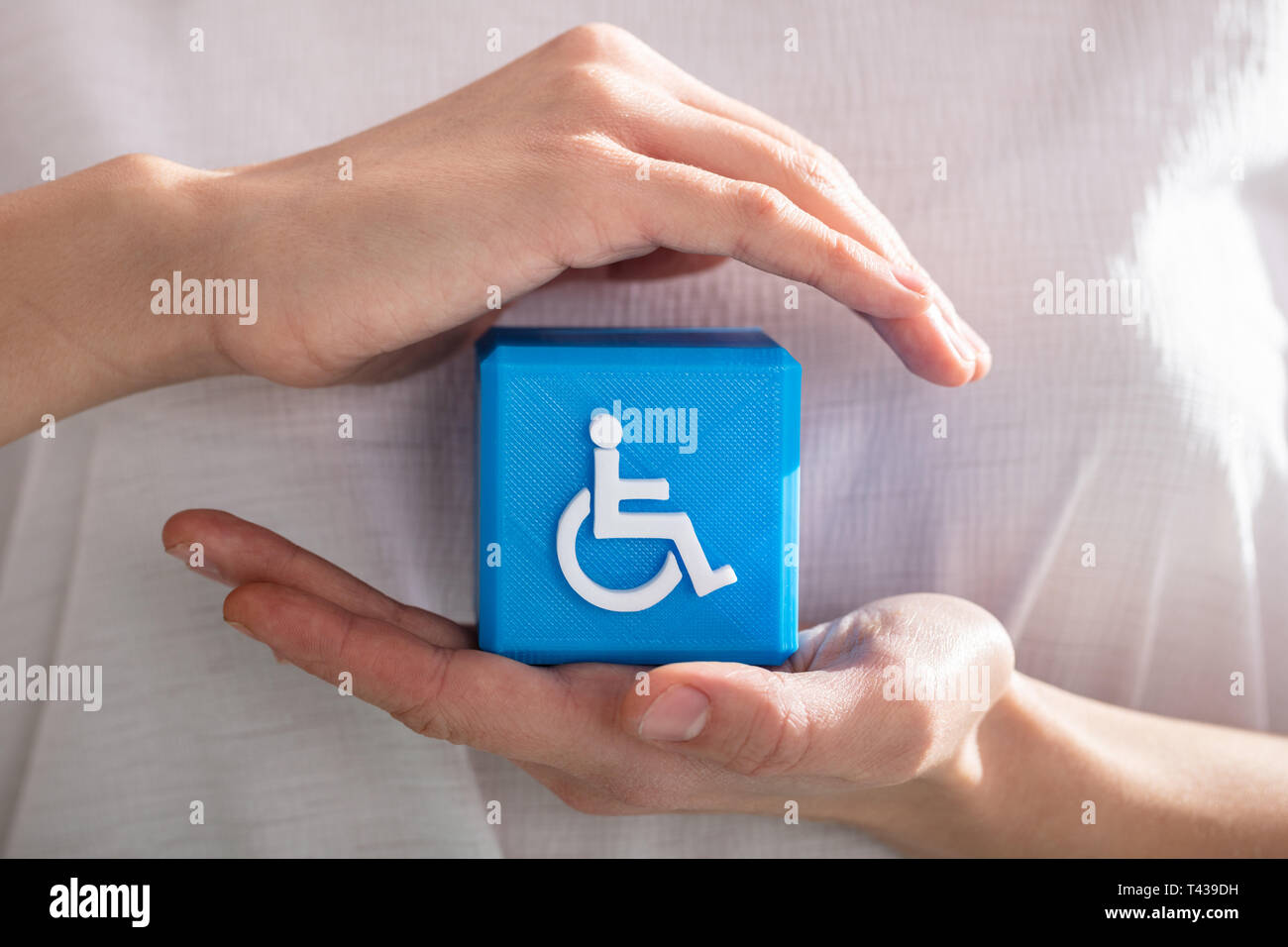 Close-up Of A Human's Hand Protecting Blue Cubic Block With Disabled Handicap Icon Stock Photo