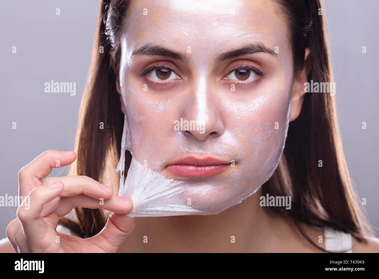 Portrait Of A Beautiful Young Woman Removing Peeling Mask From Her Face Stock Photo