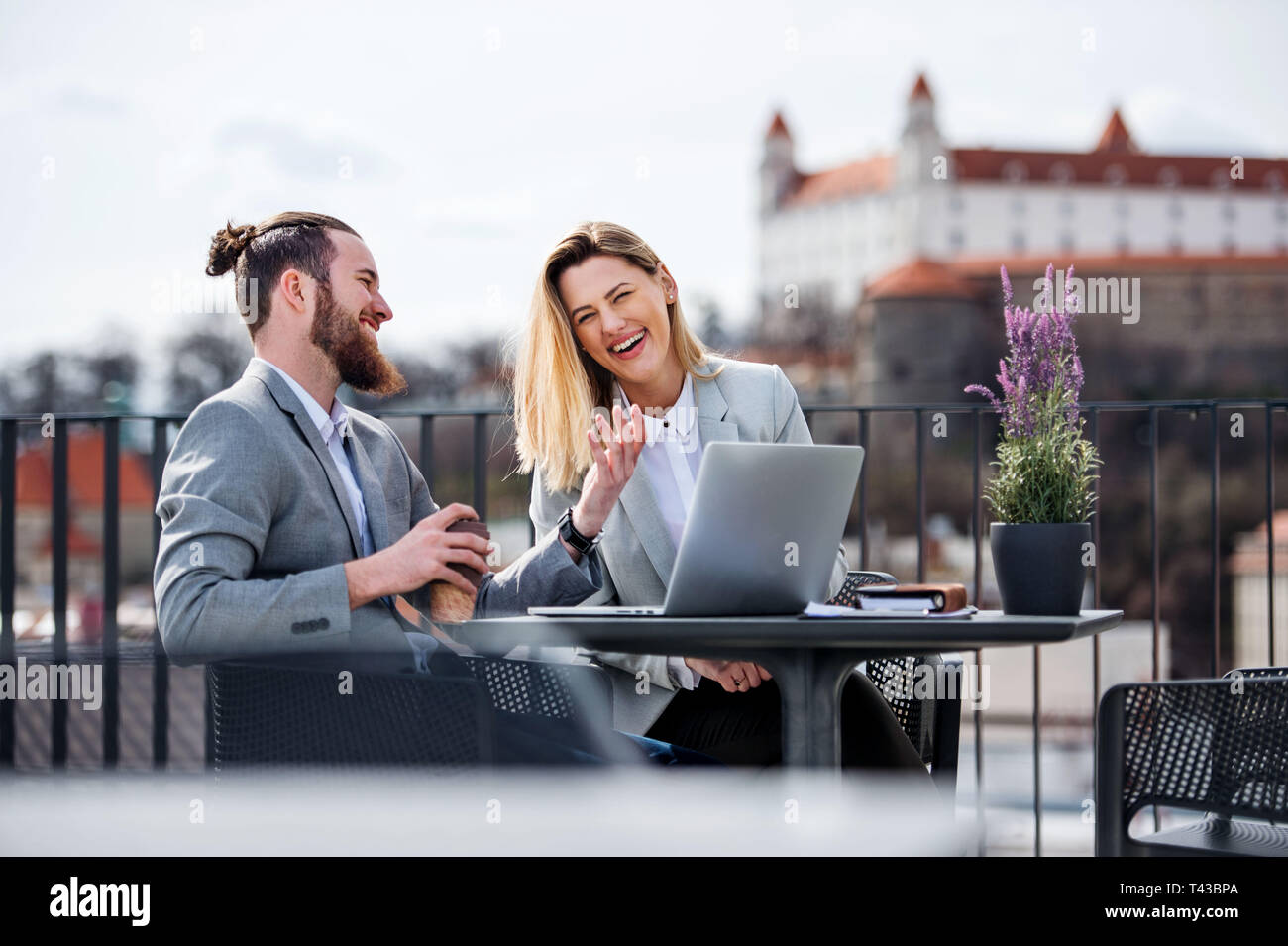 Two young business people with laptop sitting on a terrace outside office, working. Stock Photo