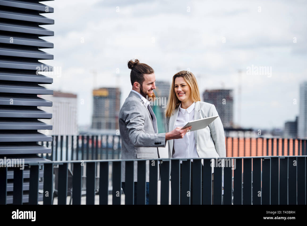 Two young business people with tablet standing on a terrace outside office, working. Stock Photo
