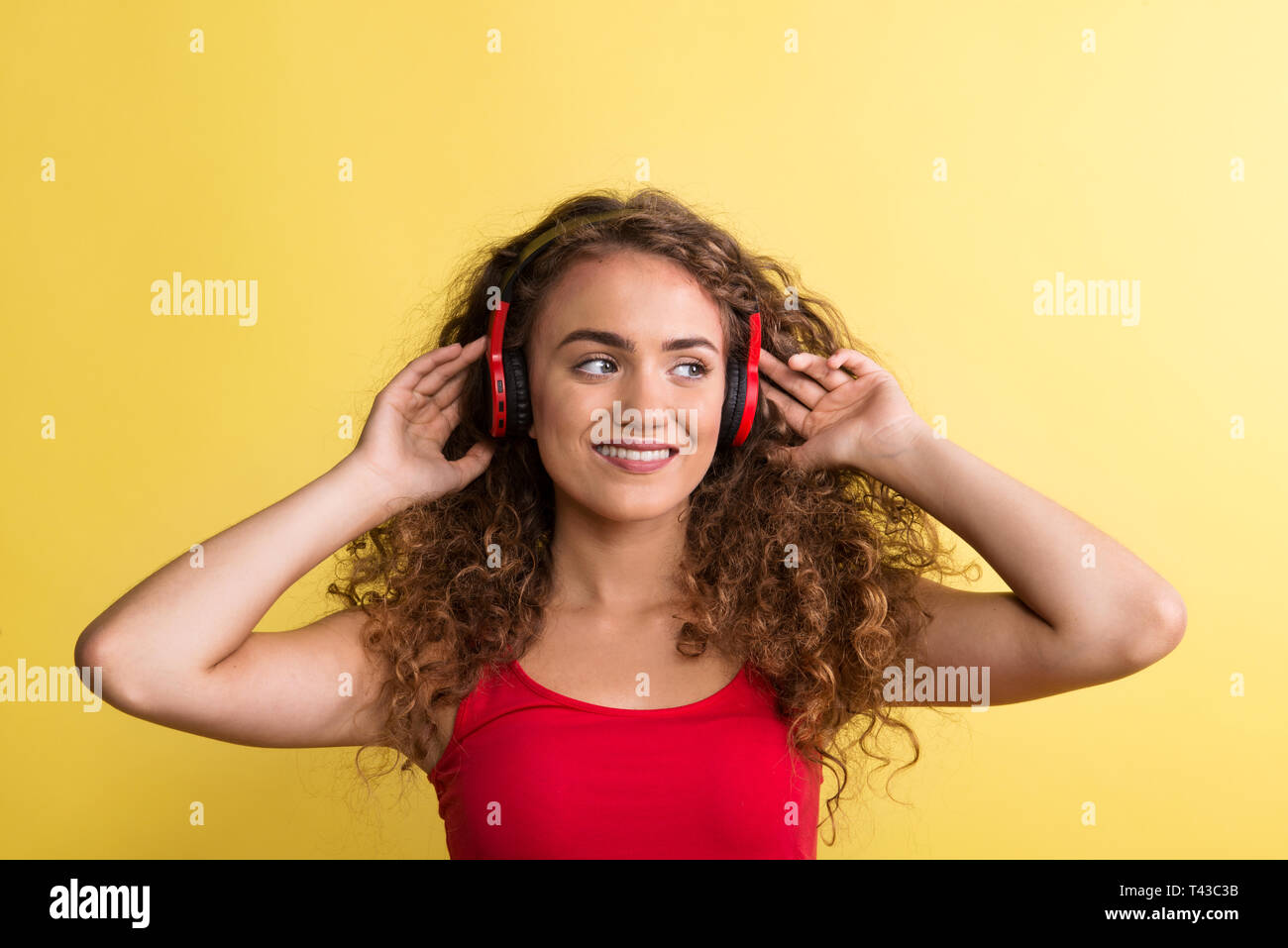 Portrait of a young woman with headphones in a studio on a yellow background. Stock Photo