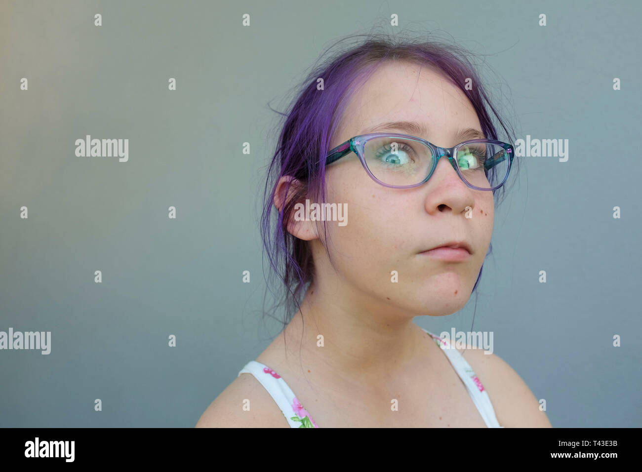 Portrait of a teenage girl with purple hair and prescription glasses and  attitude against a grey wall Stock Photo - Alamy