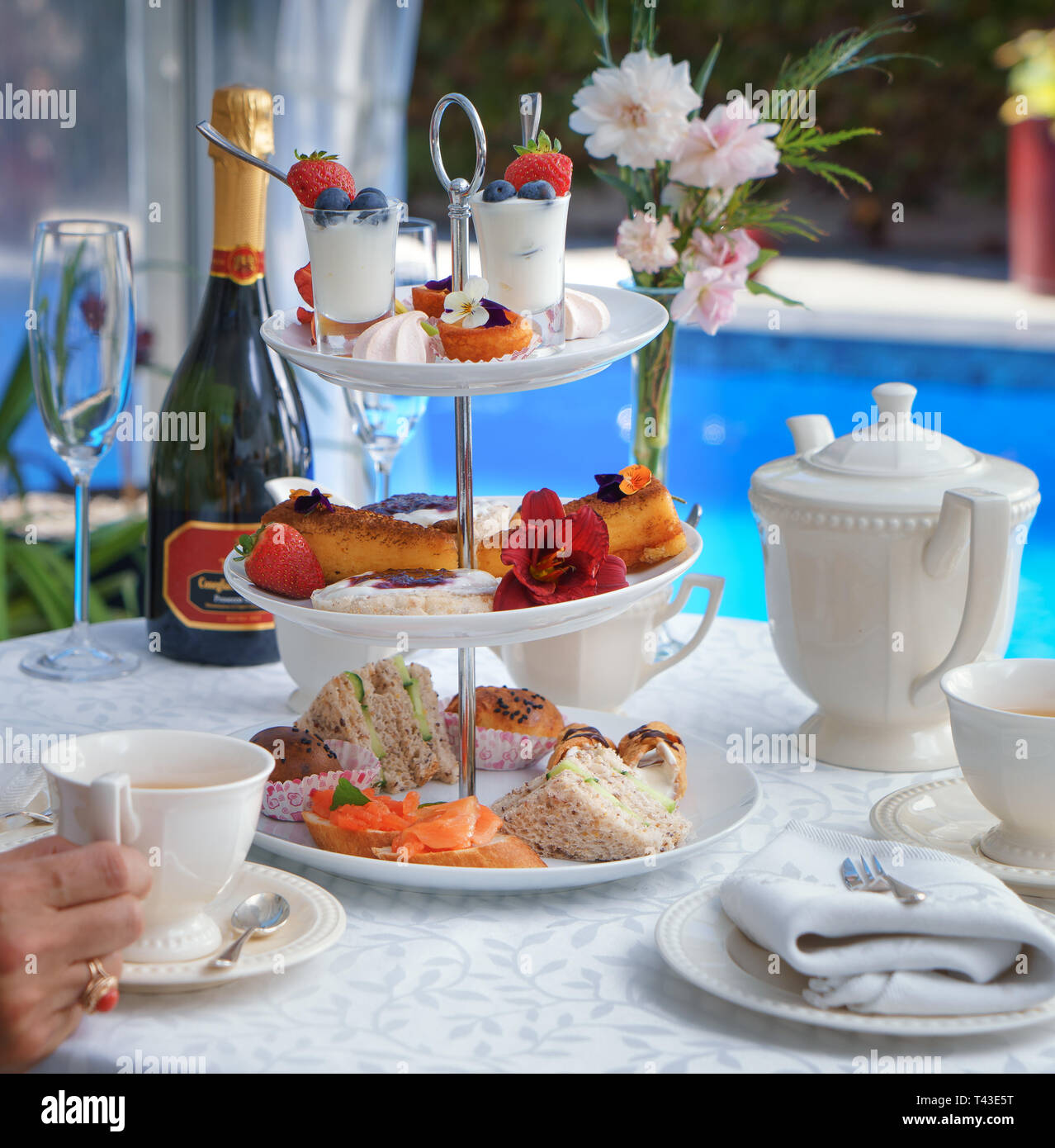 A close up of a high tea on a cake stand served with a bottle of fizz by the pool Stock Photo