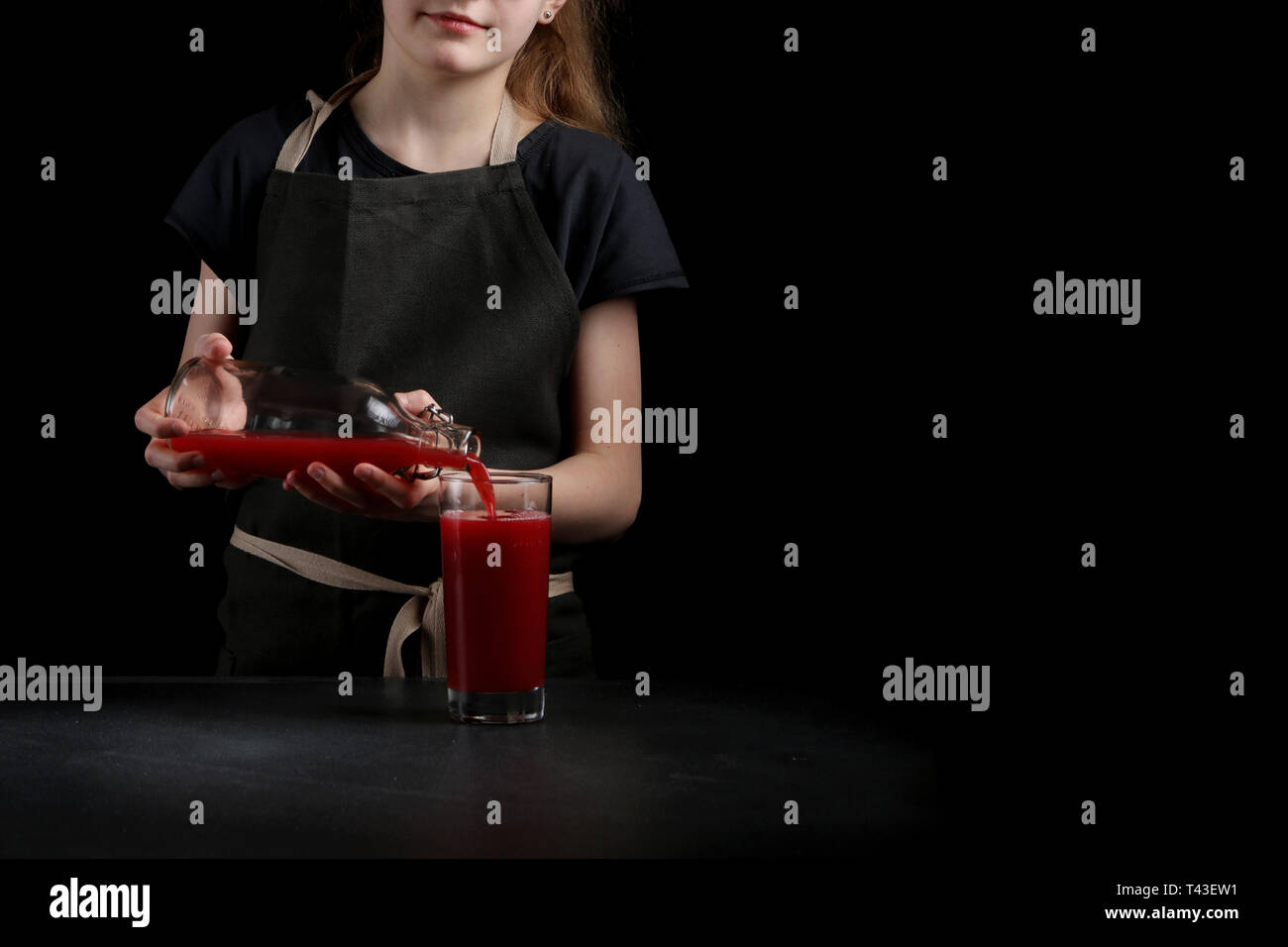 girl pouring juice in glass on dark background. summer drink concept