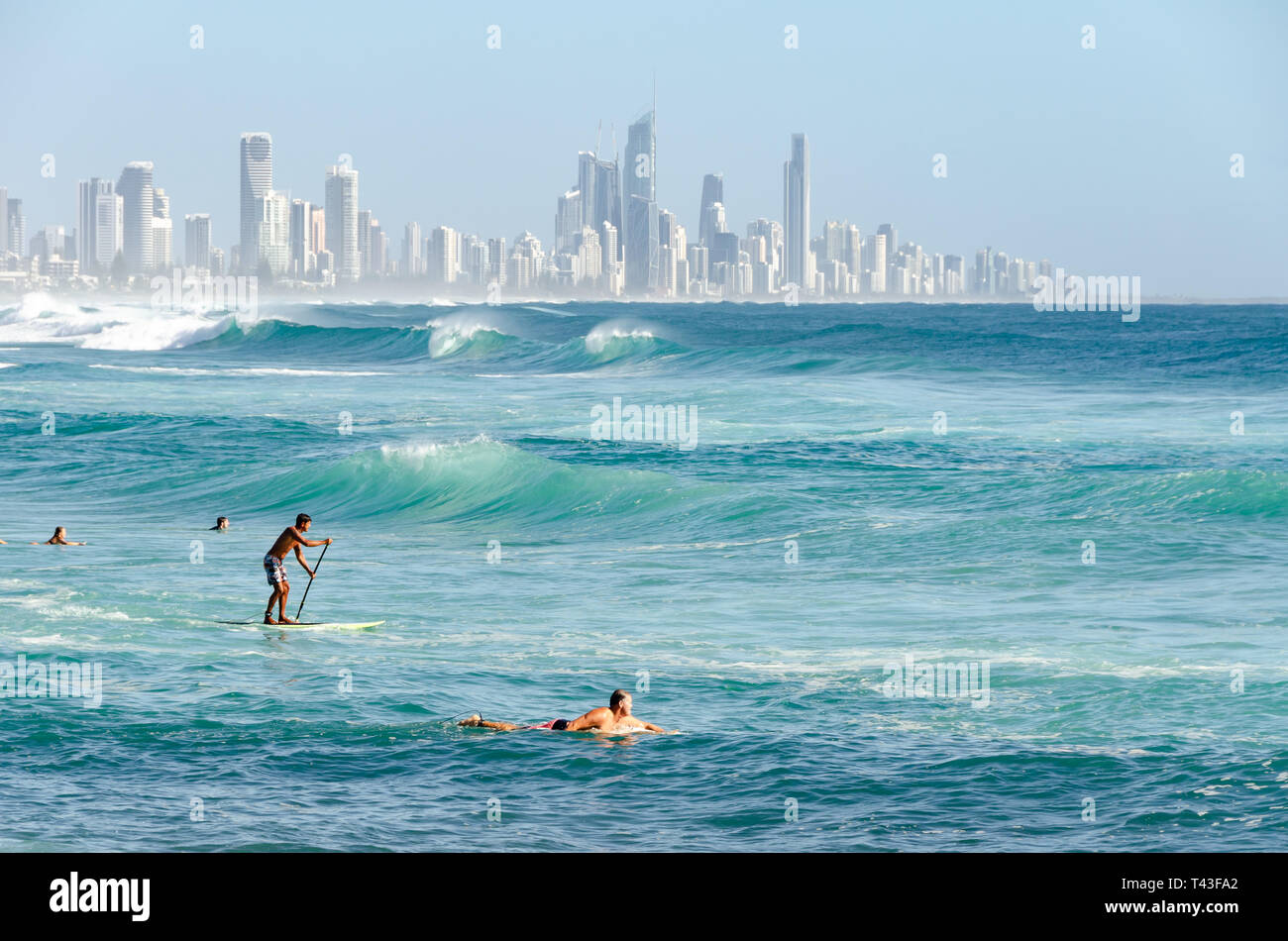 People on the beach, swimming and surfing, at Burleigh Heads, Gold Coast, Queensland, Australia.  Surfers Paradise in distance. Stock Photo