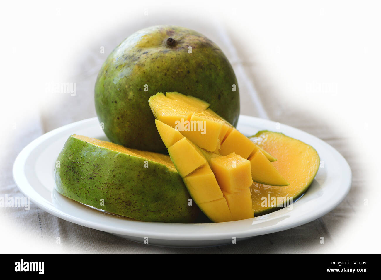 diced mango with whole fruit on side in white dish Stock Photo