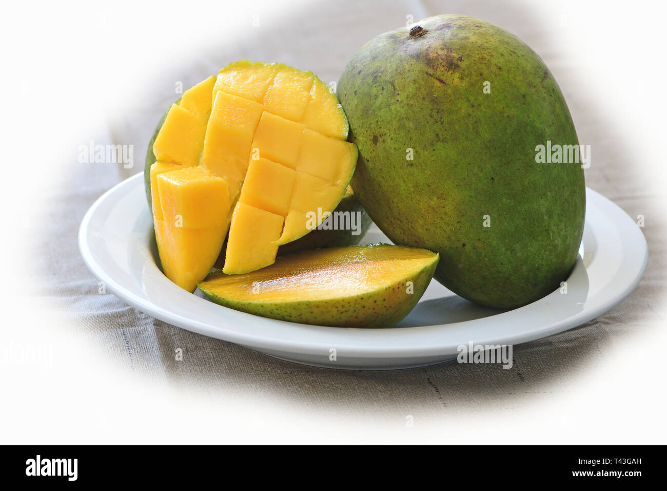 diced mango with whole fruit on side in white dish Stock Photo