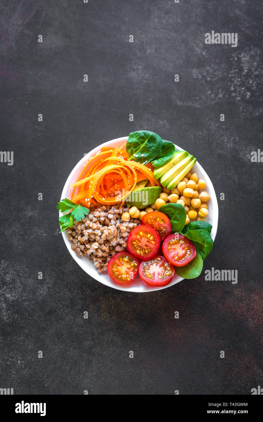 Buddha bowl salad with buckwheat, avocado, carrot, tomato, spinach, chickpea on black. Healthy vegetarian vegan diet eating, super food. Top view, cop Stock Photo