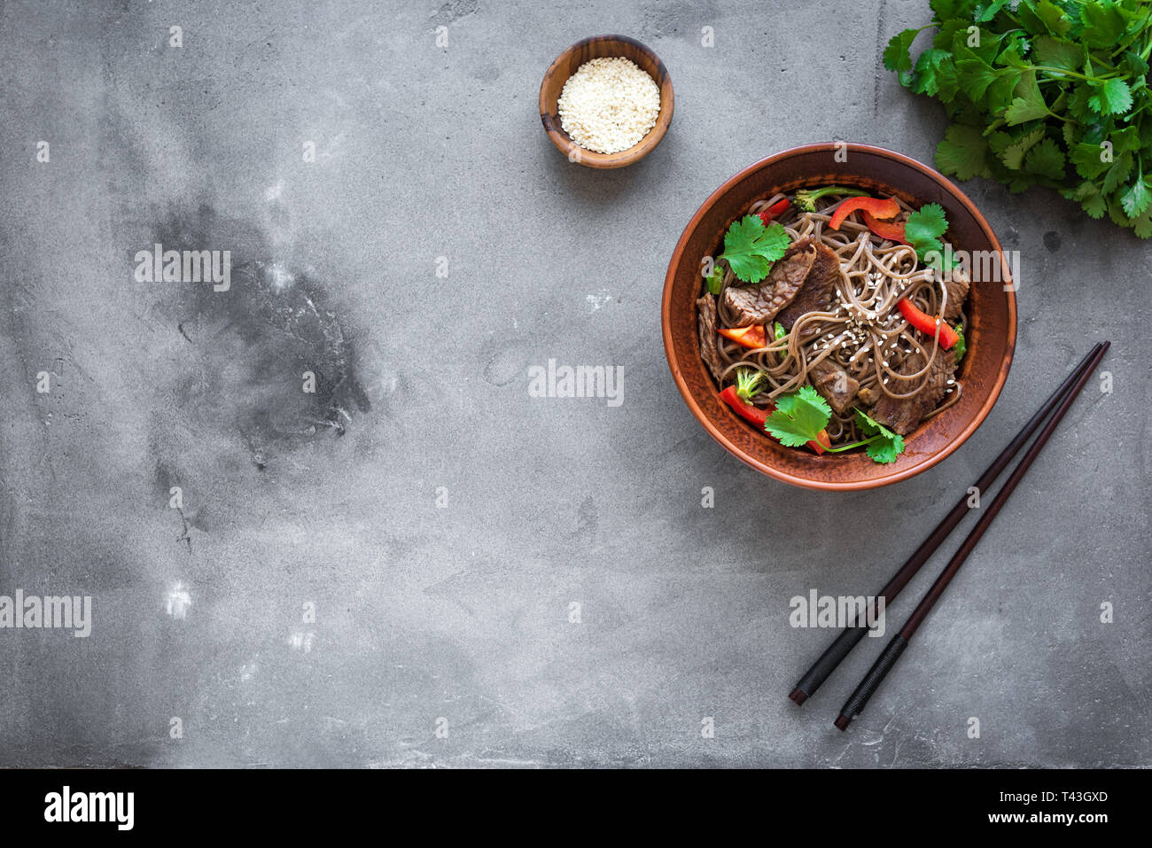 Stir fry with soba noodles, beef and vegetables. Asian healthy food, stir fried meal in bowl on dark background, top view, copy space. Stock Photo