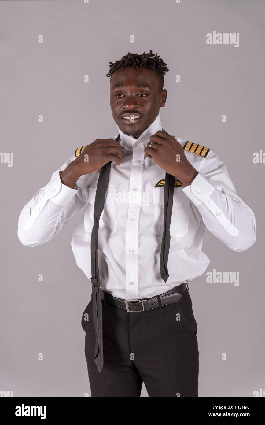 London,UK. April 2019. A young airline pilot with an african dred hairstyle.  Crew member tying his black tie Stock Photo - Alamy