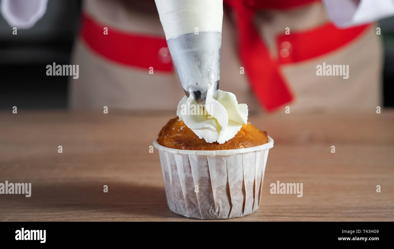 Pastry chef decorates cupcake in paper cups white cream with pastry bag