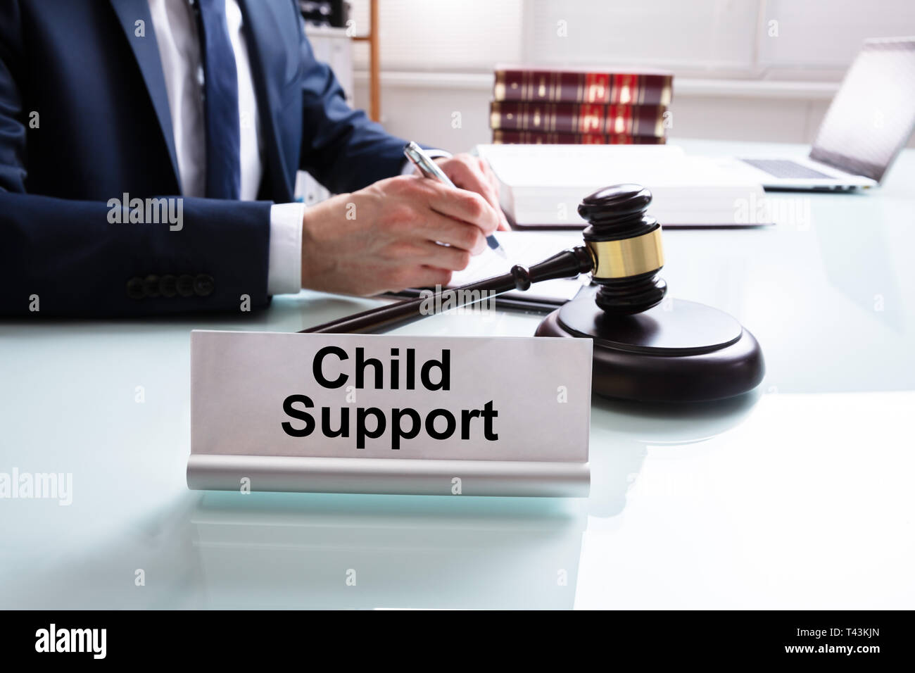 Child Support Nameplate With Judge Writing On Paper Over Desk In Courtroom Stock Photo