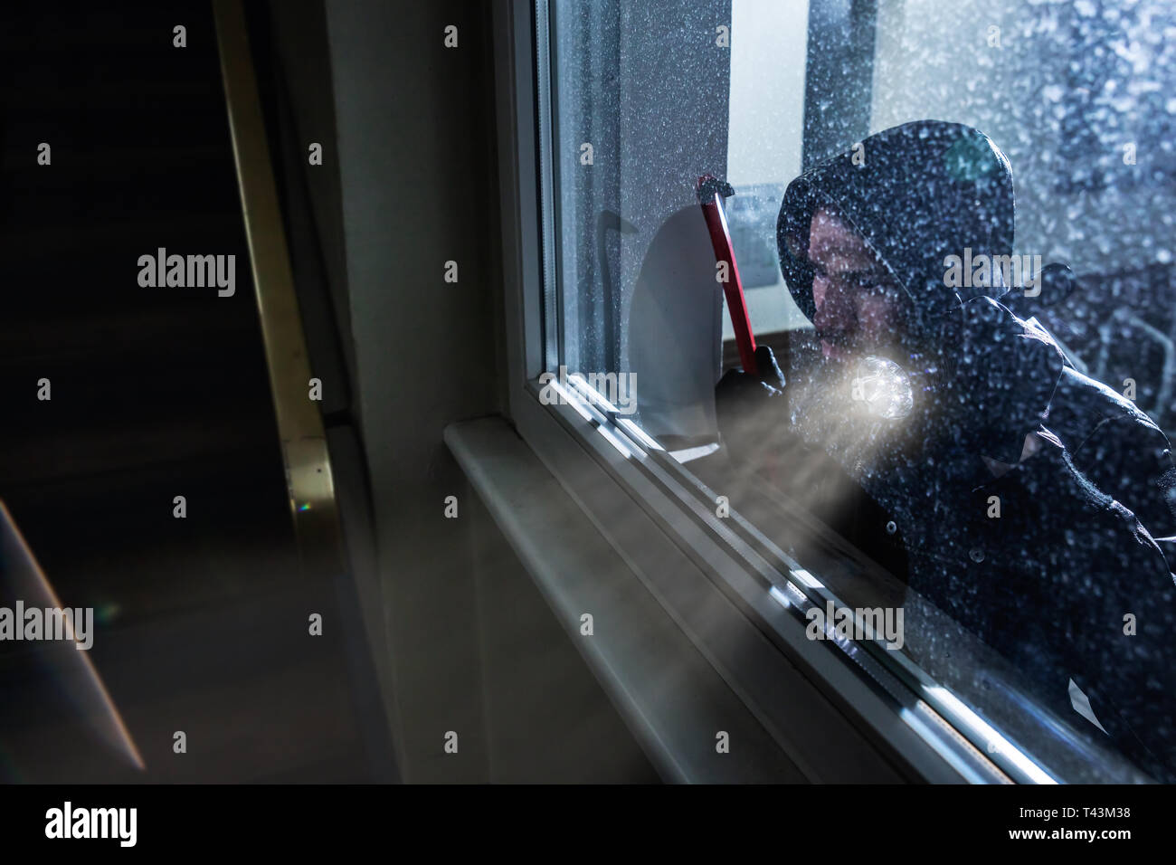 Burglar With Crowbar And Flashlight Looking Into A House Windows Stock Photo