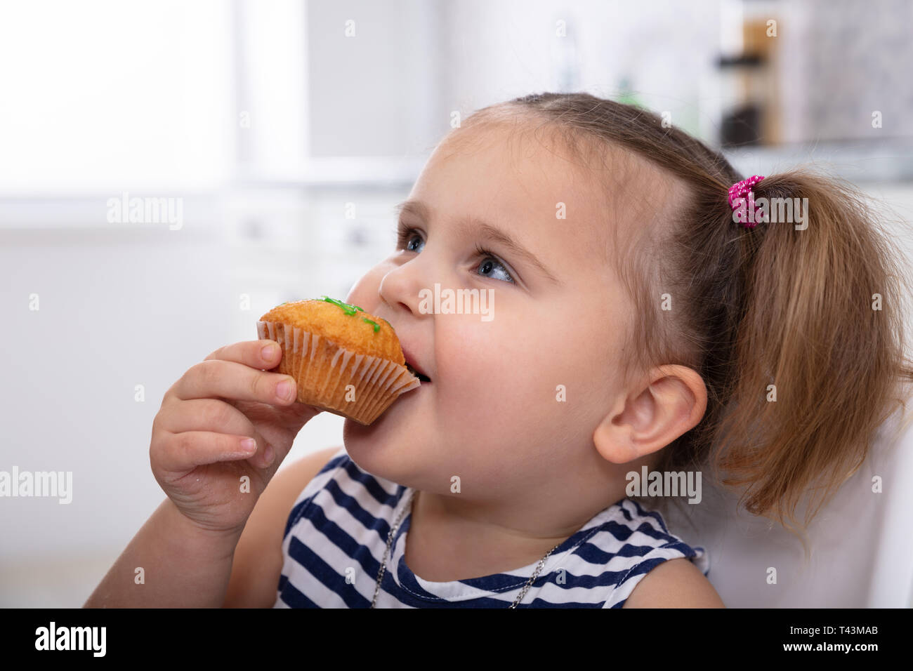 Happy Innocent Girl Taking A Bite Of Delicious Cupcake In The Kitchen Stock Photo