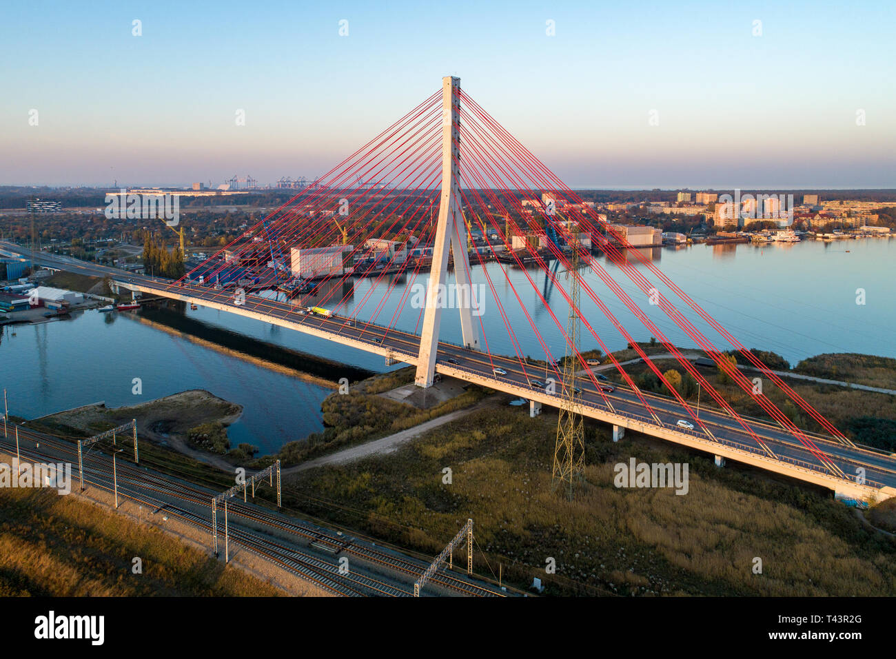 Gdansk, Poland. Modern highway cable-stayed bridge over Dead Vistula river and the railway.. Aerial view in sunset light. Northern Port  far in the ba Stock Photo