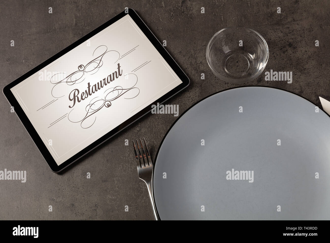 Tablet with stylish restaurant logo and laid table Stock Photo