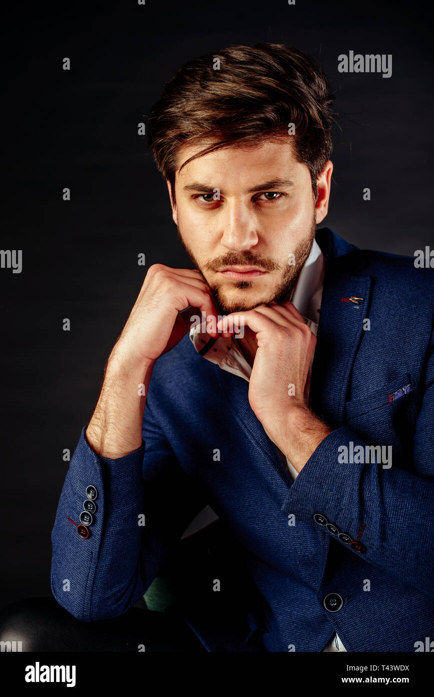 Handsome young elegant man in blue suit pose against studio background ...