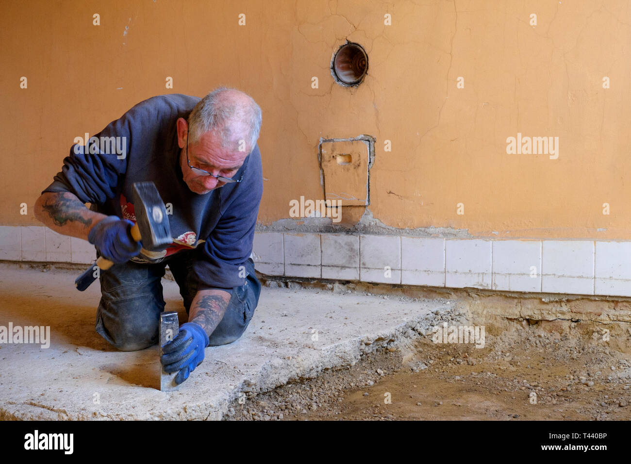 man using hammer and chisel to dig up concrete floor during house