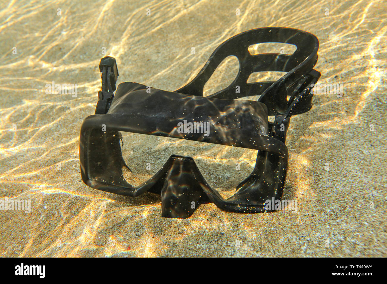 Underwater photo - light from sun refractions at black diving mask sitting in shallow water on clear sand Stock Photo