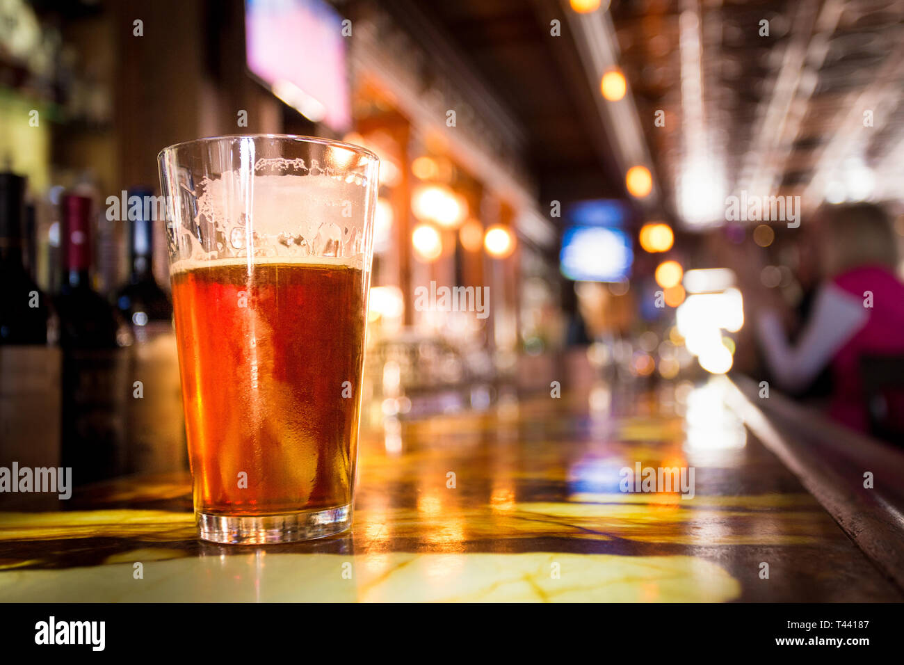 Glass Pint of amber beer with colorful blur of bar in background Stock