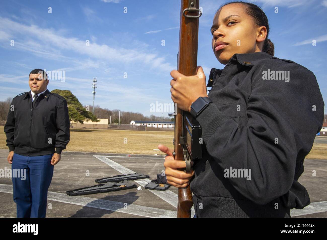 Firing party commander U.S. Army Spc. Aldo A. Posas, left, stands at attention as Pfc. Janee S. Simpler, both members of the New Jersey National Guard Honor Guard, prepares to fire her M-14 rifle during three-Soldier firing party training at the parade field at the National Guard Armory in Lawrenceville, N.J., March 14, 2019. During this practice, the Soldiers reviewed the sequence of events for a full honors firing detail, which includes a series of three volleys fired in honor of the deceased veteran by the honor guard. The three volleys represent the words duty, honor, and country.  (New Je Stock Photo