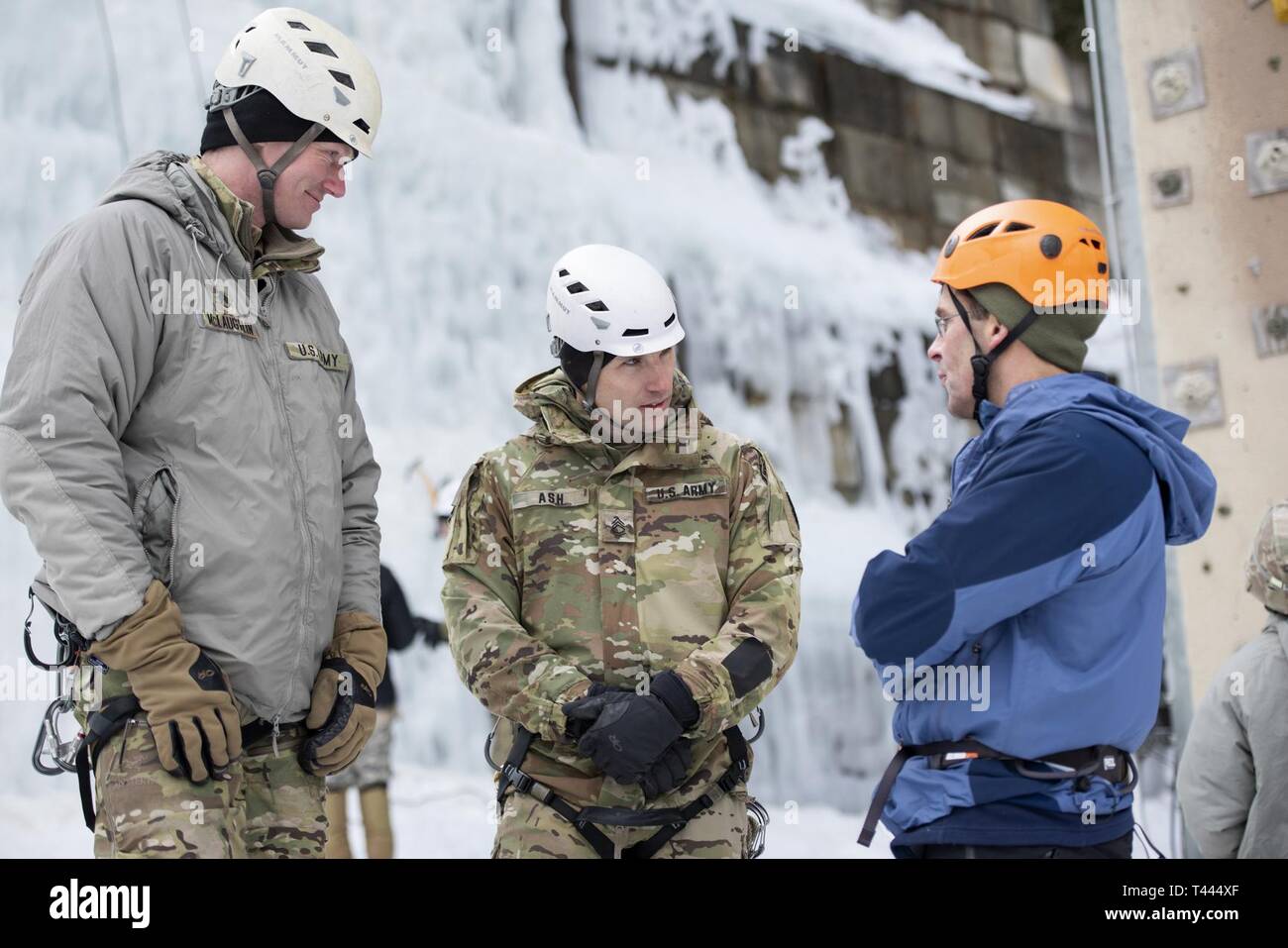 U.S. Army Staff Sgt. Timothy MCLaughlin, left and Staff Sgt. Nick Ash, both instructors with the Army Mountain Warfare School, speak with Secretary of the Army Dr. Mark T. Esper at the Army Mountain Warfare School on Camp Ethan Allen Training Site, Jericho, Vt., March 16, 2019. Esper was able to observe and visit with students currently in the both the Basic Military Mountaineering Course and Advanced Military Mountaineering Course. Stock Photo