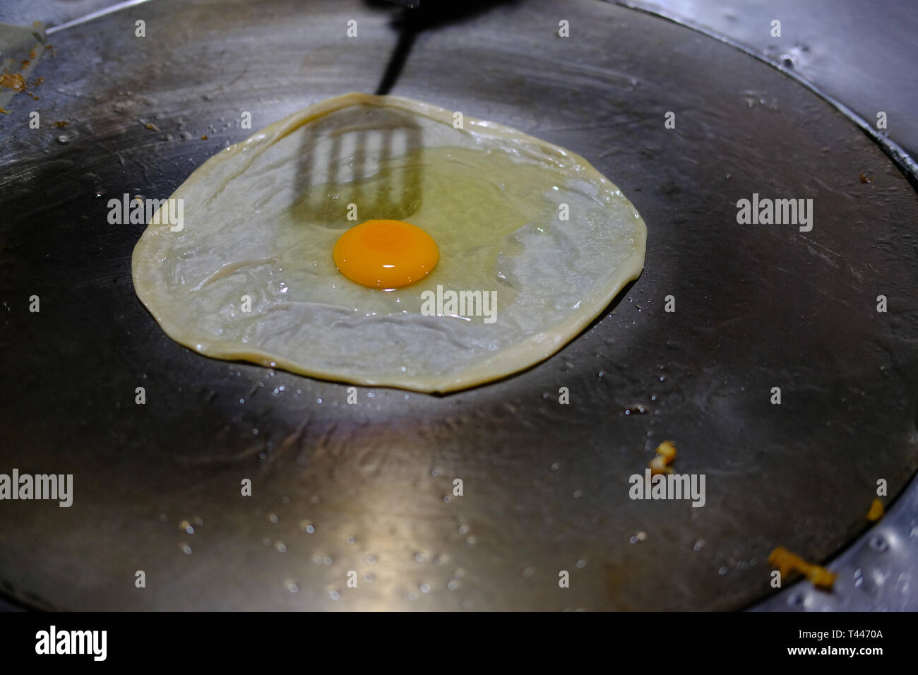 frying egg on roti on hot pan. traditional street food in Thailand Stock Photo