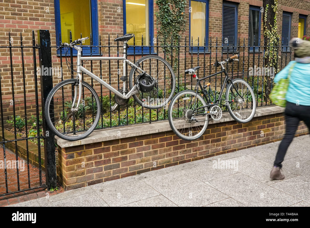 Old bicycles locked to metal fence, high above ground, blurred person passing by on pavement Stock Photo